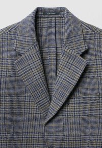 Blazer in lana con un motivo a quadri blu, grigio e verde. Dettagli notevoli includono un colletto a punta e rever strutturati.