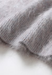 Tessuto in maglia grigia chiara, morbido e percettibile al tatto; presenta leggere variazioni di tonalità e un motivo a coste lungo il bordo.