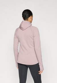 Sweatshirt com capuz cor de rosa claro, de ajuste justo, apresentando uma textura suave, mangas raglan e capuz com cordão. Combinado com leggings pretas.