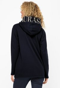 Felpa navy con un grande logo chiaro sulla cappuccio, caratterizzata da una texture morbida e una vestibilità rilassata, vista da dietro.