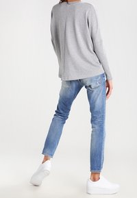 Top grigio a maniche lunghe con cucitura posteriore, abbinato a jeans azzurri strappati e scarpe da ginnastica bianche, che mostrano un outfit casual.