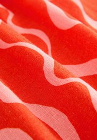 Textiel, oranje stof met golvende, roze patronen. De textuur lijkt glad met een fijne structuur en heeft een zachte, vloeiende val.