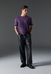 Camisa corta de manga corta morada, textura suave, combinada con pantalones amplios de cuero negro y zapatos negros con cordones. Diseño simple, fondo neutro.