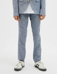 Világoskék len anyagú öltöny, textúrázott felülettel, amelyhez szűk fazonú nadrág és hozzáillő zakó tartozik, fehér és fekete sportcipővel párosítva.