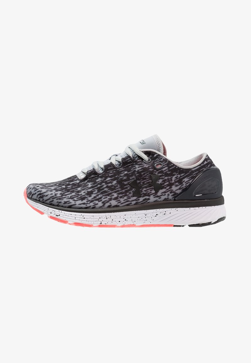 Chaussure de sport noire et grise à motif, avec des lacets blancs, un logo Under Armour noir, une semelle blanche mouchetée et des accents corail sur la semelle extérieure.