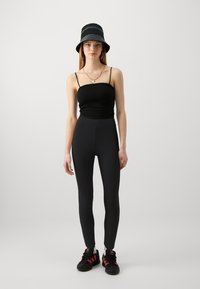 Un débardeur noir, un legging noir taille haute et des baskets noires avec des accents rouges ; portant un chapeau seau noir et rayé, avec des bijoux minimalistes.