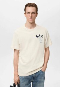T-shirt in cotone crema con maniche corte, con la scritta "M.V.P." in blu sul petto, abbinata a jeans di denim blu.