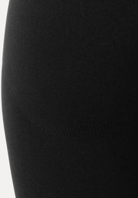 Gros plan sur un tissu noir extensible avec une texture subtile côtelée et un modelage des contours sur une surface lisse.