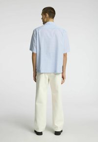 Šviesiai mėlynas ir baltas kartotinės medžiagos marškinėliai trumpomis rankovėmis, pagaminti iš medvilnės. Stiliai su laisvomis kreminėmis kelnėmis ir juodais batais.