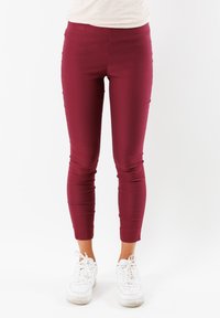 Leggings bordeaux in tessuto elasticizzato, design aderente e caviglie affusolate, abbinati a scarpe da ginnastica bianche. Texture liscia su tutta la superficie.