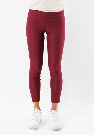Leggings bordeaux in tessuto elasticizzato, design aderente e caviglie affusolate, abbinati a scarpe da ginnastica bianche. Texture liscia su tutta la superficie.