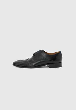 Svart skinn herresko i oxford-stil med brogue-detaljer og lisser, vist i profil mot en nøytral grå bakgrunn.