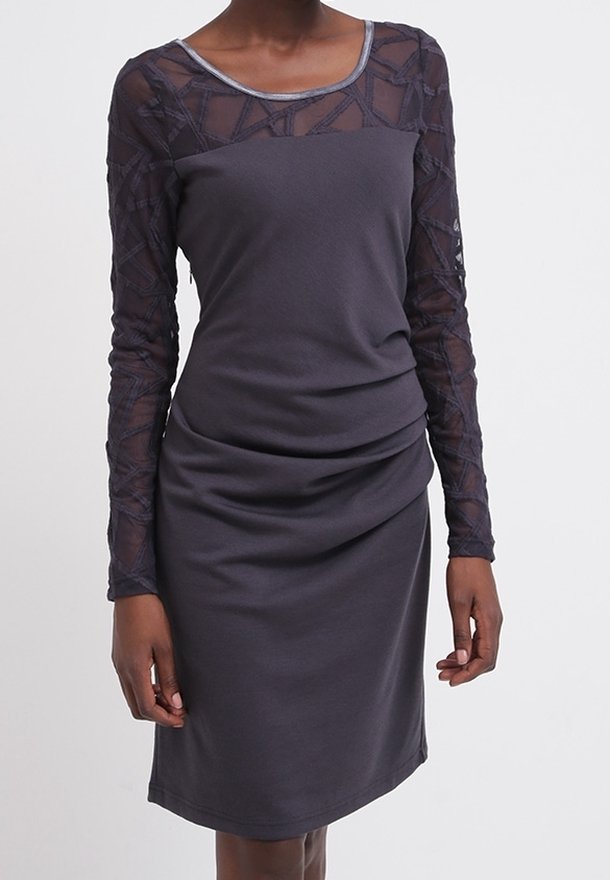 Femme portant une robe gris foncé longueur genou avec des manches longues transparentes à motifs et un décolleté rond.