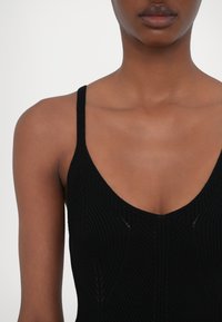 Svart ribbestrikket tanktop med tynne skulderstropper og lav V-hals, med teksturerte vertikale linjer og et åpent sømdesign.