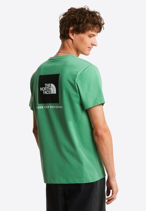 Camiseta de algodón verde con un gráfico cuadrado negro que muestra el texto "THE NORTH FACE" y "NEVER STOP EXPLORING" en la parte trasera. Mangas cortas.