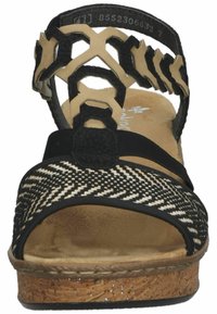 Zwarte en beige wedge sandaal met een geweven patroon, verstelbare band, gevoerd voetbed en kurkachtige zool. Open teenontwerp.