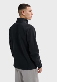 Czarny polarowy sweter z wysokim kołnierzem, długimi rękawami i gładką teksturą. Posiada prosty dół i minimalne szwy.