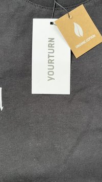 Musta orgaanilisest puuvillast T-särk tekstuuriga viimistlusega, millel on õmmeldud silt "YOURTURN" ja beež silt, mis näitab "ORGANIC COTTON".