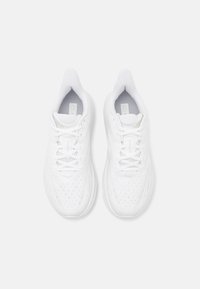 Zapatillas deportivas blancas con parte superior de malla, puntera redonda y suela acolchada. Cordones y logo visibles en la lengüeta. Textura perforada en toda la superficie.