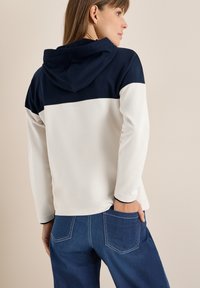 Felpa con cappuccio caratterizzata da una parte superiore blu navy e una parte inferiore crema, realizzata in tessuto morbido con vestibilità ampia e maniche con polsini.