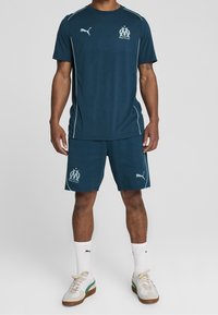 L'outfit atletico navy comprende una maglietta a maniche corte e pantaloni sportivi, entrambi con dettagli del logo. Realizzato in materiale leggero con una consistenza liscia.