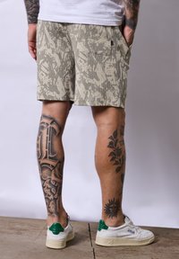 Be�żowo-szare spodenki w kamuflażu z teksturowanej tkaniny, z bocznymi kieszeniami i luźnym krojem. Noszone z białymi sneakersami.