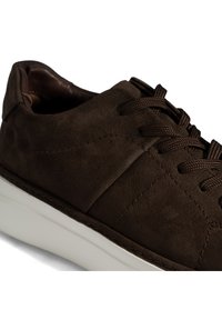 Braune Ledersneaker mit strukturiertem Obermaterial, runder Zehenpartie, flacher weißer Sohle und kontrastierenden braunen Schnürsenkeln mit dezenten Nahtdetails.