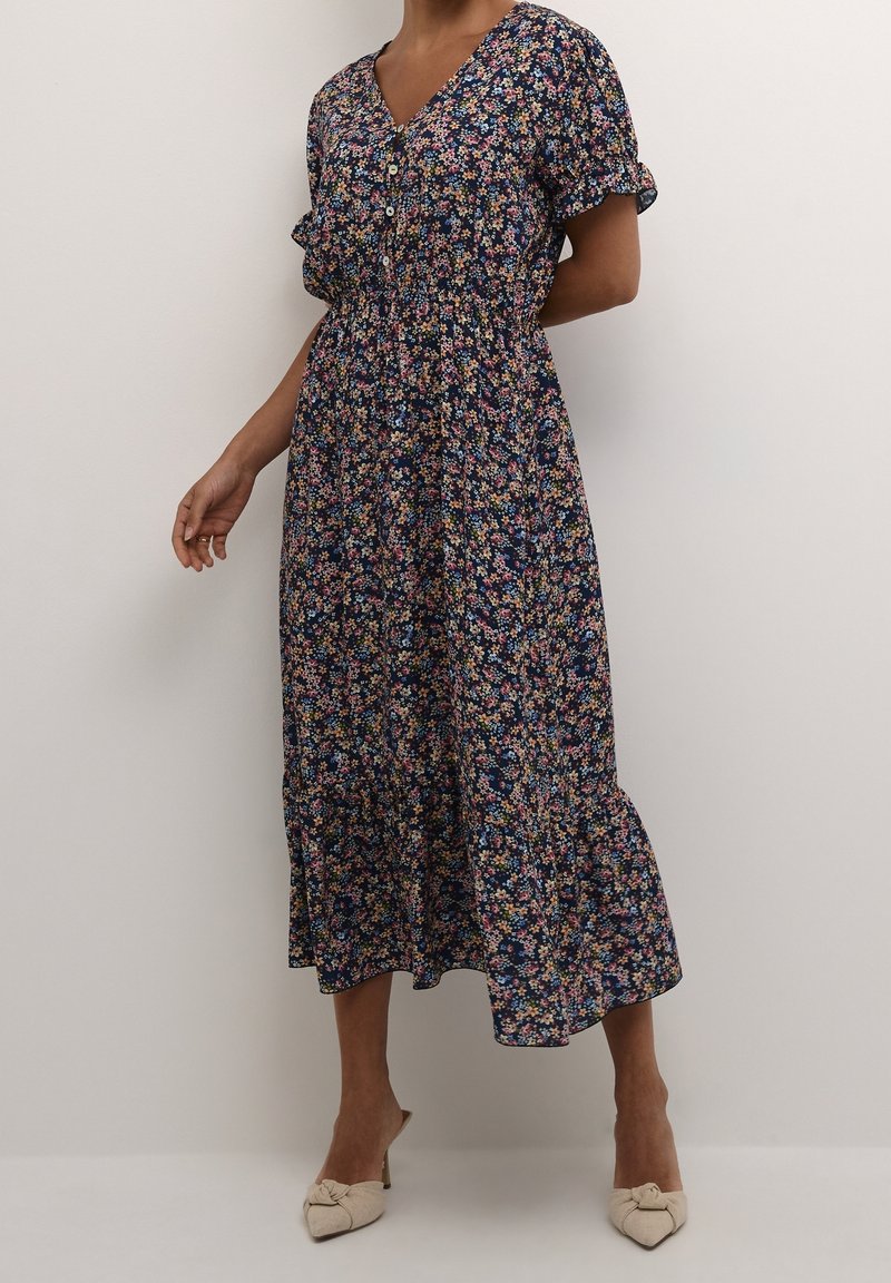 Robe midi florale avec un fond bleu marine, manches courtes à volants, décolleté en V, détails à boutons et ourlet évasé. Petites fleurs multicolores partout.
