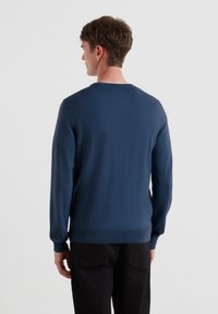 Granatowy sweter z długimi rękawami, prążkowanymi mankietami i dołem oraz okrągłym dekoltem. Gładka tekstura, dopasowany fason i minimalne zdobienia.