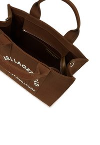 Brūna auduma soma ar divām rokām. Iekšpusē ir rāvējslēdzēja kabata un kontrastējoša odere. Priekšpusē ir balts zīmola nosaukums.