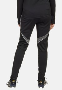 Schwarze Sporthose mit slim fit, die silberne Akzente und seitliche Reißverschlüsse aufweist. Hergestellt aus einem dehnbarem Material für Komfort und Bewegungsfreiheit.