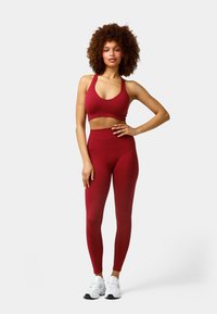 Sujetador deportivo rojo de atletismo combinado con mallas rojas de tiro alto. El material parece elástico con un mínimo detalle de costura. Zapatillas blancas completan el look.