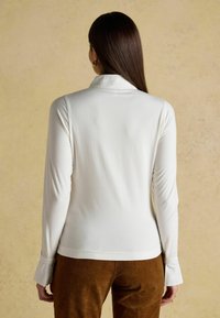 White long-sleeve top with a fitted silhouette and a soft texture. It features a standard collar and cuffed sleeves, worn with brown corduroy pants.