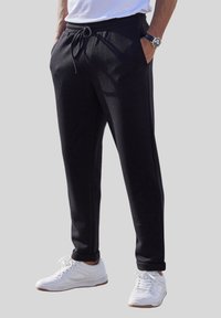 Schwarze Sweatpants aus weichem Stoff mit einem elastischen Bund, Kordelzug und zwei Seitentaschen, kombiniert mit weißen Turnschuhen.