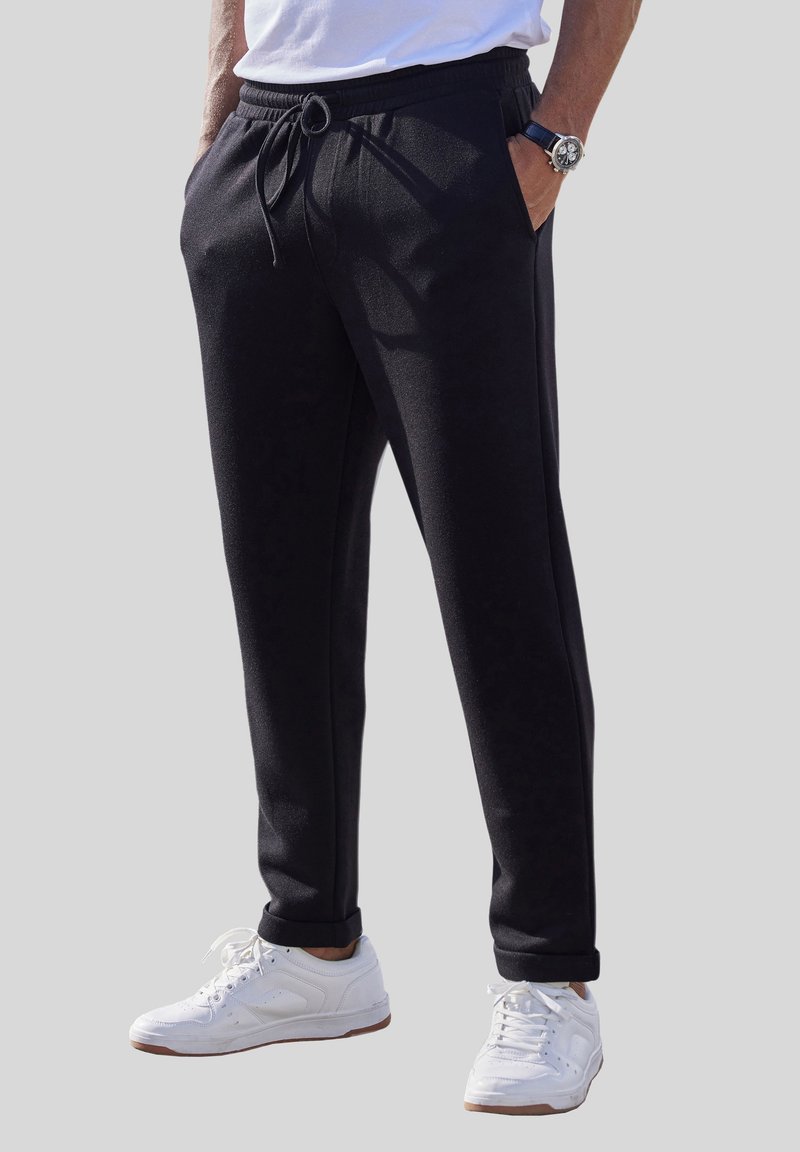 Schwarze Sweatpants aus weichem Stoff mit einem elastischen Bund, Kordelzug und zwei Seitentaschen, kombiniert mit weißen Turnschuhen.