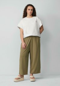 T-shirt blanc à manches courtes avec broderie florale, associé à un pantalon fluide vert olive et des sandales à plateforme beiges. Design simple et décontracté.