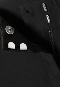 Tissu noir à la texture lisse avec un bouton rond, deux clips argentés et une fermeture éclair dissimulée.