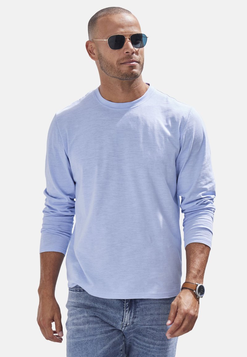 Himmelblaues Langarmshirt mit Rundhalsausschnitt, weichem Material, kombiniert mit Jeans und runden Sonnenbrillen, das einen lässigen Look präsentiert.