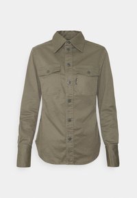 Olivgrön knapp-up skjorta i bomull, med spridd krage, två bröstfickor, svarta knappar och rundad nederkant.