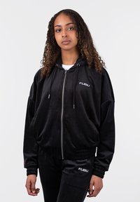 Juodas veliūro džemperis su užtrauktuku ir reguliuojamomis virvutėmis, turintis priekinę kišenę ir išsiuvinėtą "FUBU" logotipą ant krūtinės. Derinamas su kelnėmis.