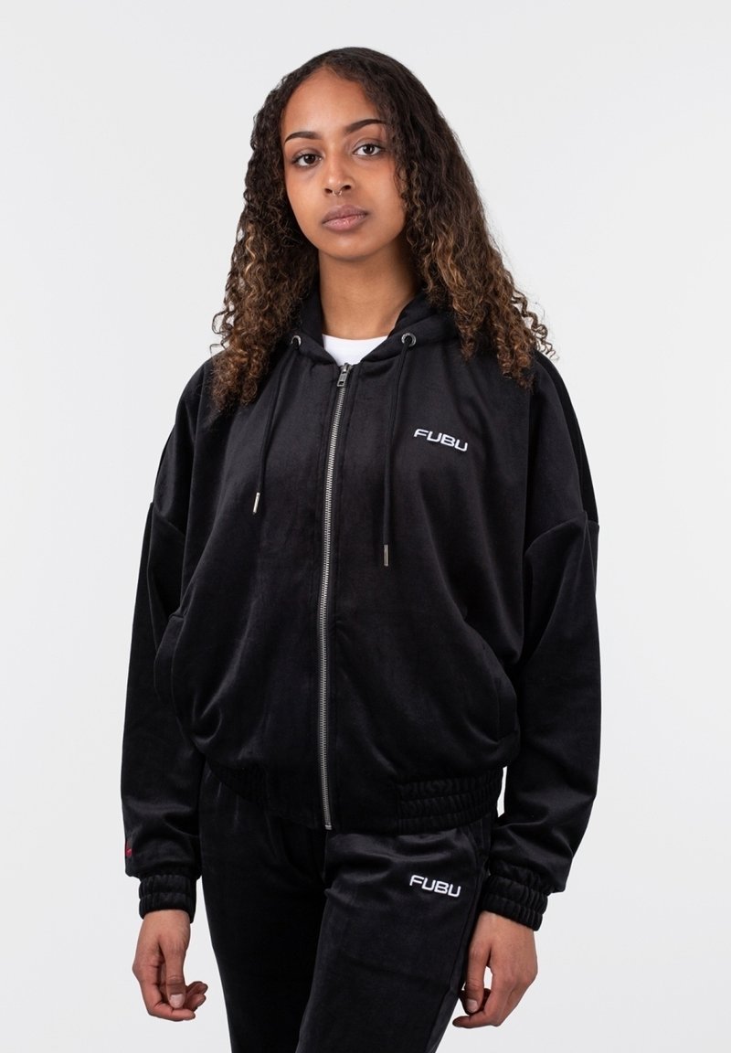 Juodas veliūro džemperis su užtrauktuku ir reguliuojamomis virvutėmis, turintis priekinę kišenę ir išsiuvinėtą "FUBU" logotipą ant krūtinės. Derinamas su kelnėmis.
