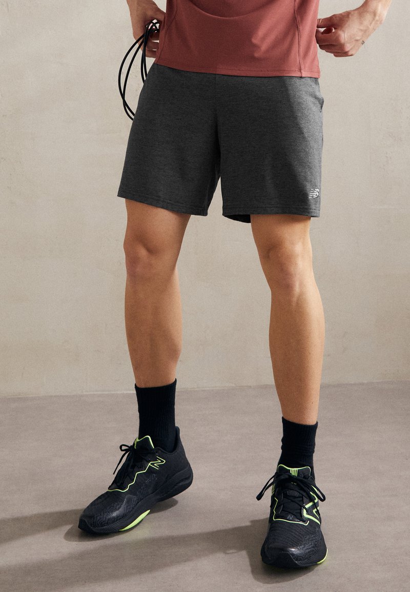 Shorts de sport pour homme de couleur gris foncé en tissu léger, associés à des chaussures de course noires avec des accents vert néon et des chaussettes noires unies.