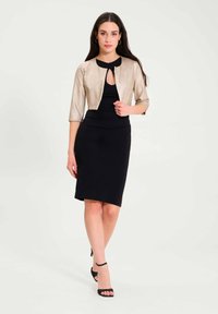 Metallic gold cropped jacket over a black fitted dress. Jacket features three-quarter sleeves and a keyhole detail at the neckline. Black heels.