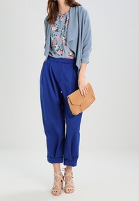 Ljusblå, draperad cardigan över en blommig blus; lösa, livfulla blå byxor; en tan clutch och beiga klackskor med remmar fulländar looken.