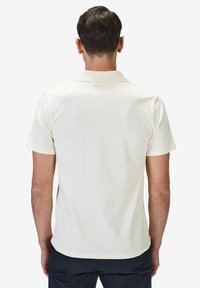 Kortärmad pikétröja i ljus krämfärg, i bomullsblandat material, med klassisk krage och en mjuk textur. Enkel design utan mönster.