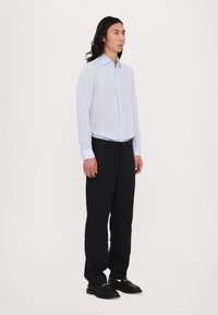 Himmelblaues, langärmliges Hemd mit Knopfleiste aus strukturiertem Stoff; kombiniert mit schwarzen, maßgeschneiderten Hosen und schwarzen Schuhen. Minimalistisches Design.