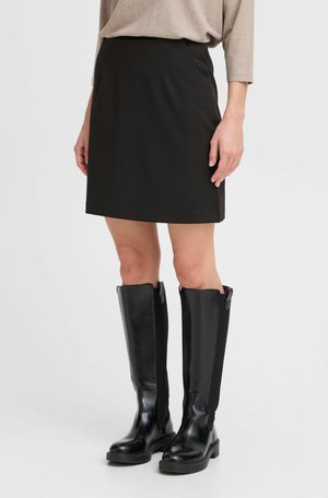 Mini-jupe noire avec poches latérales, associée à des bottes noires montantes présentant un cuir verni et des panneaux élastiques pour un design ajusté.