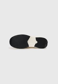 Suela de goma negra con patrón de agarre texturizado y entresuela blanca. Presenta un diseño curvado y una ranura central para mayor flexibilidad.