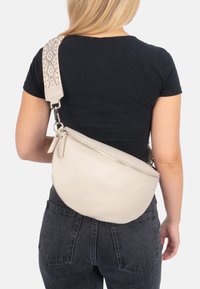 Beige Leder Umhängetasche mit strukturiertem Finish, einem einzigen Reißverschluss und einem verstellbaren gemusterten Riemen.