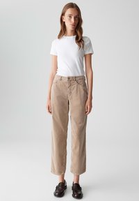 Pantaloni in corduroy beige chiaro con un design a gamba dritta, dotati di tasche frontali e chiusura con bottone, abbinati a una T-shirt bianca semplice.